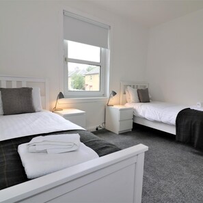 A bedroom with two beds, white headboards, and bedside tables with lamps. - Shawburn House Hamilton (Hamilton)