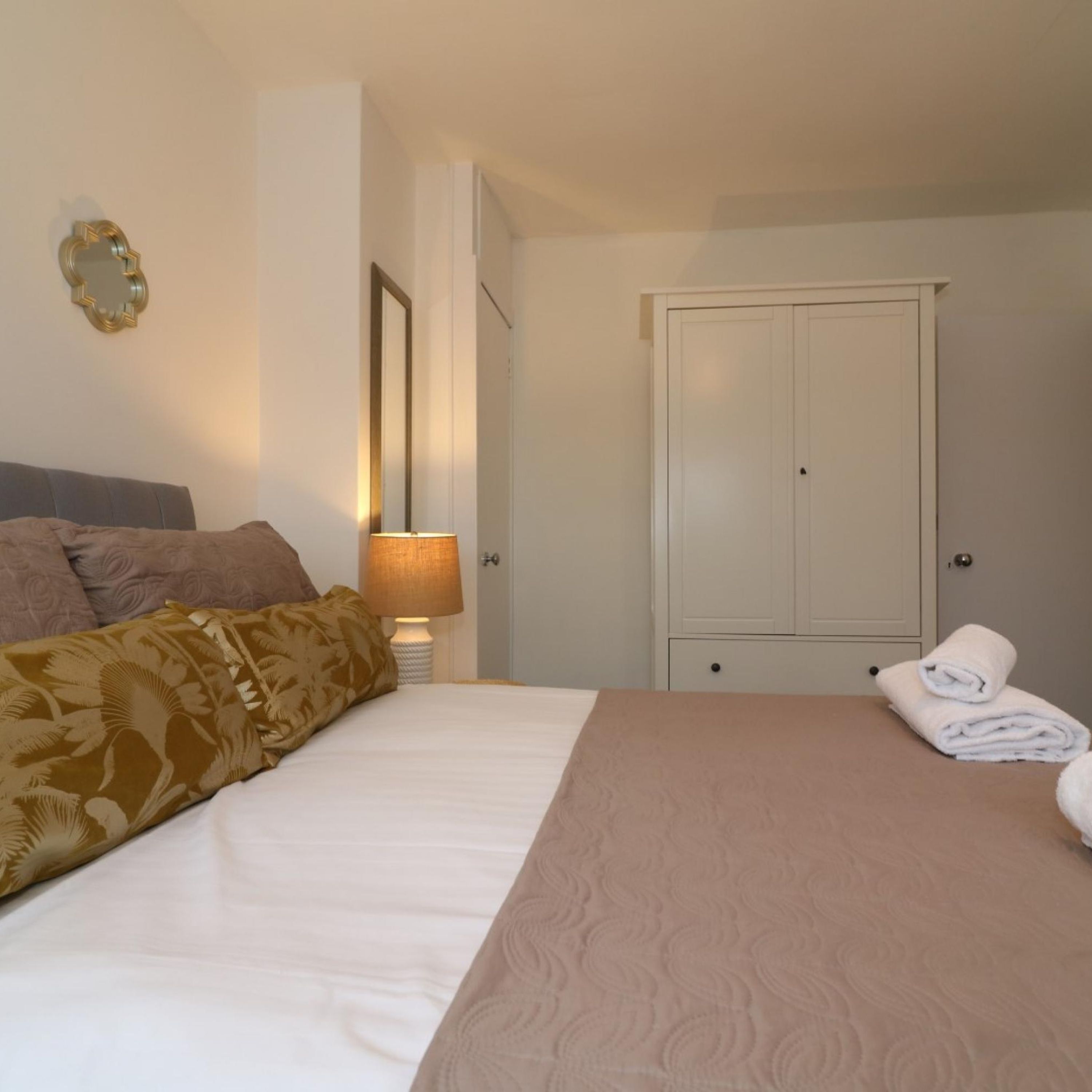 A bedroom with a bed, a wardrobe, a mirror, and a lamp.