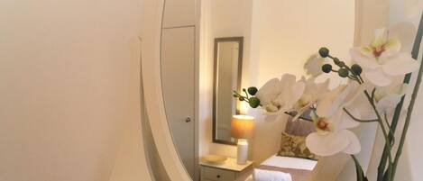 A bathroom vanity with a large mirror, a potted orchid, and a decorative leaf.