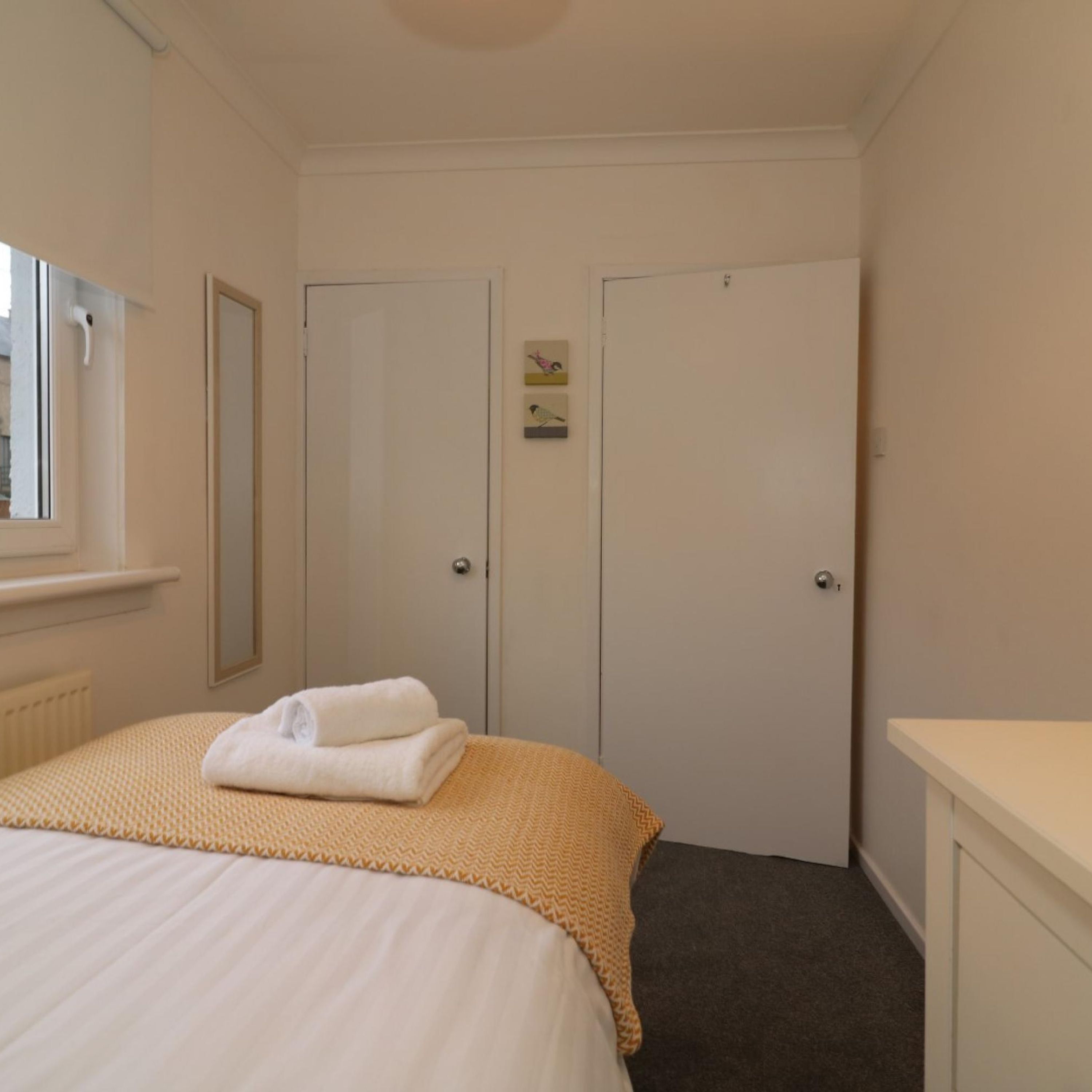 Un dormitorio con cama, dos puertas, un radiador y una ventana.