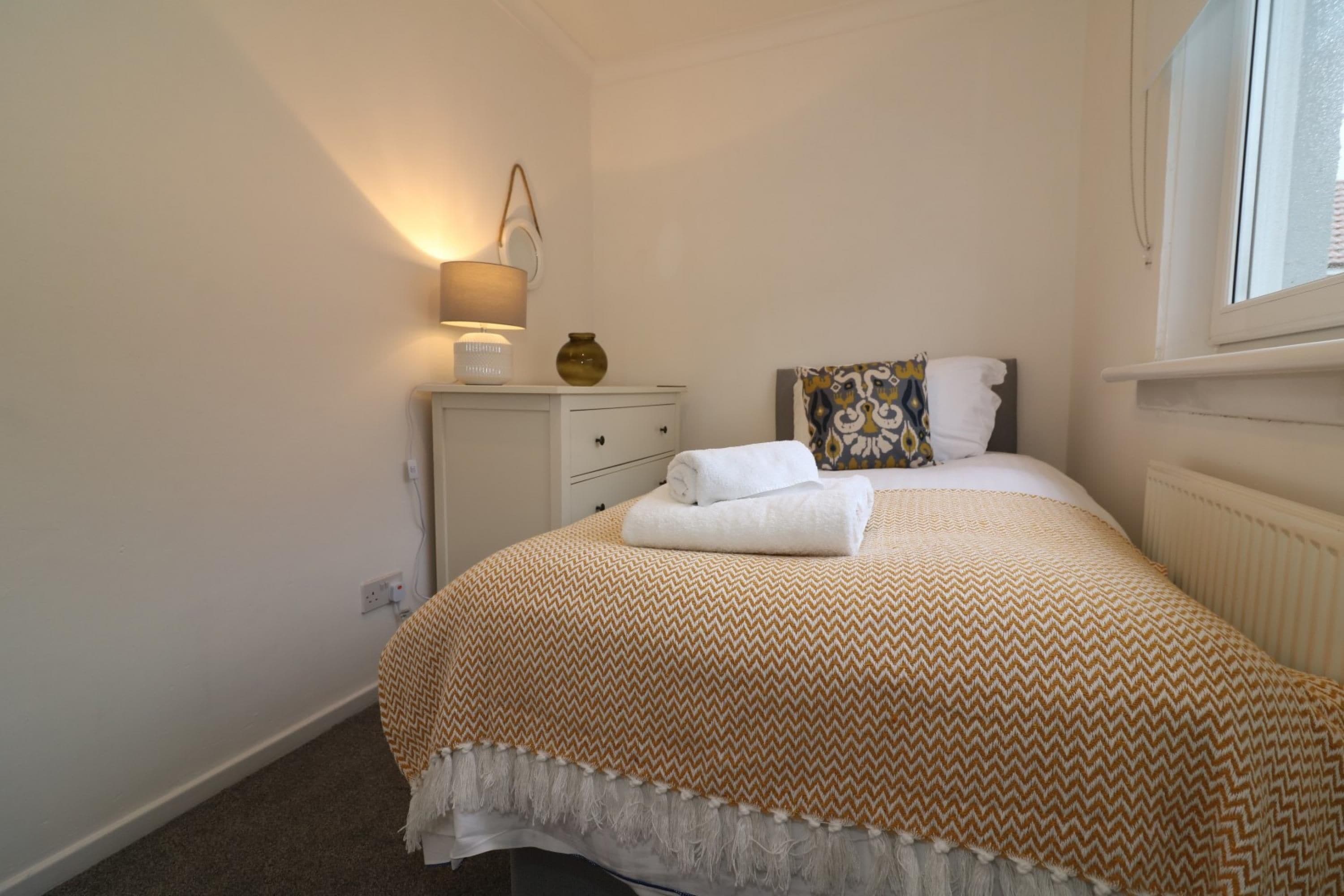 A bedroom with a bed, a bedside table, a lamp, and a window.