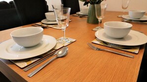 A dining table set with white plates, bowls, cutlery, and a vase with pink flowers.