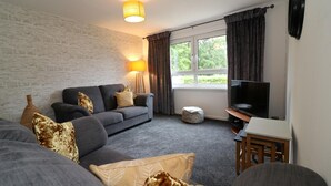 A living room with a grey sofa, a TV, and a lamp.