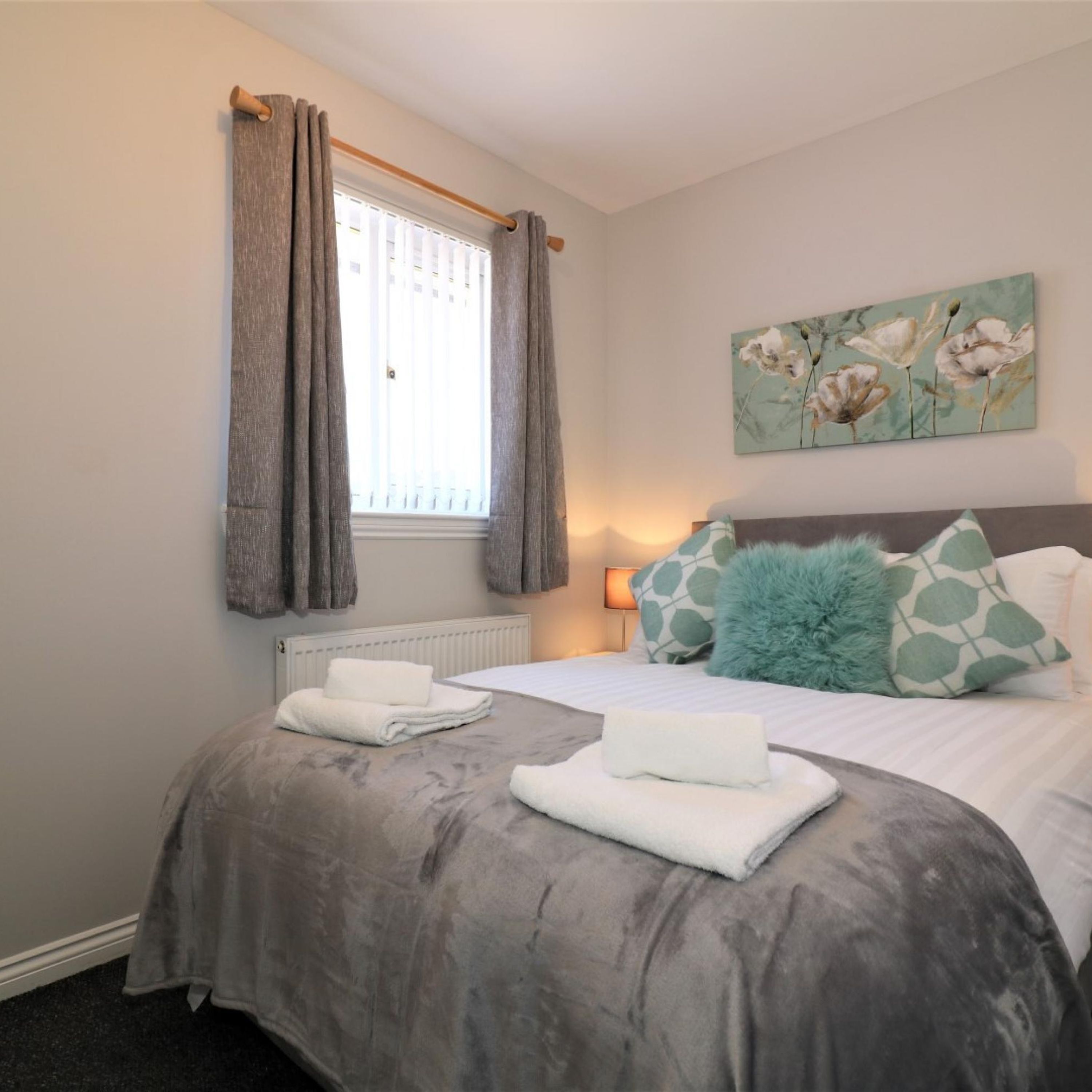 A bedroom with a bed, grey curtains, a radiator, a painting, and a fluffy pillow.