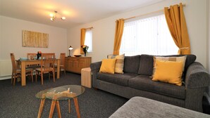 A living room with a grey sofa, wooden dining table, and glass coffee table. - Connelly House - Motherwell (Motherwell)