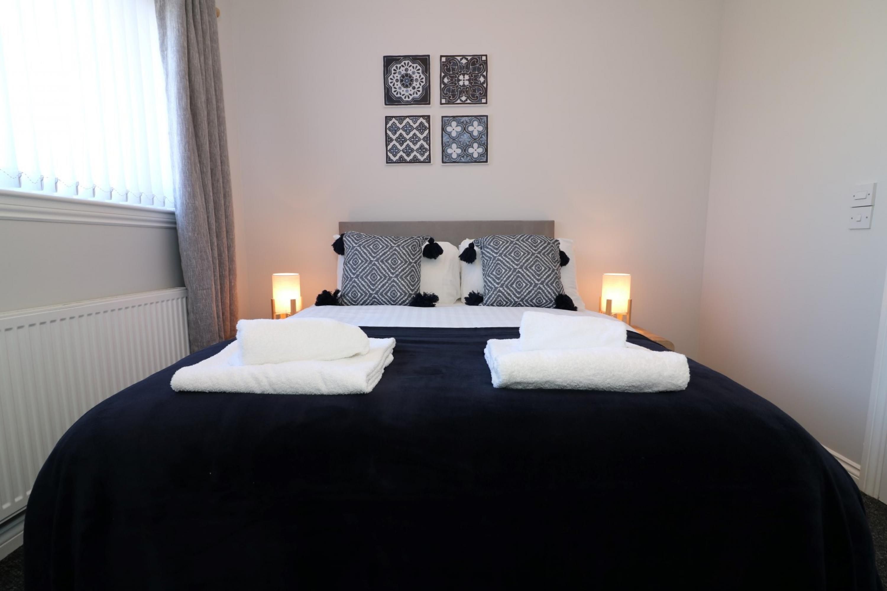 Una cama bien hecha con dos almohadas, dos lámparas de noche y un conjunto de cuatro cuadros enmarcados.