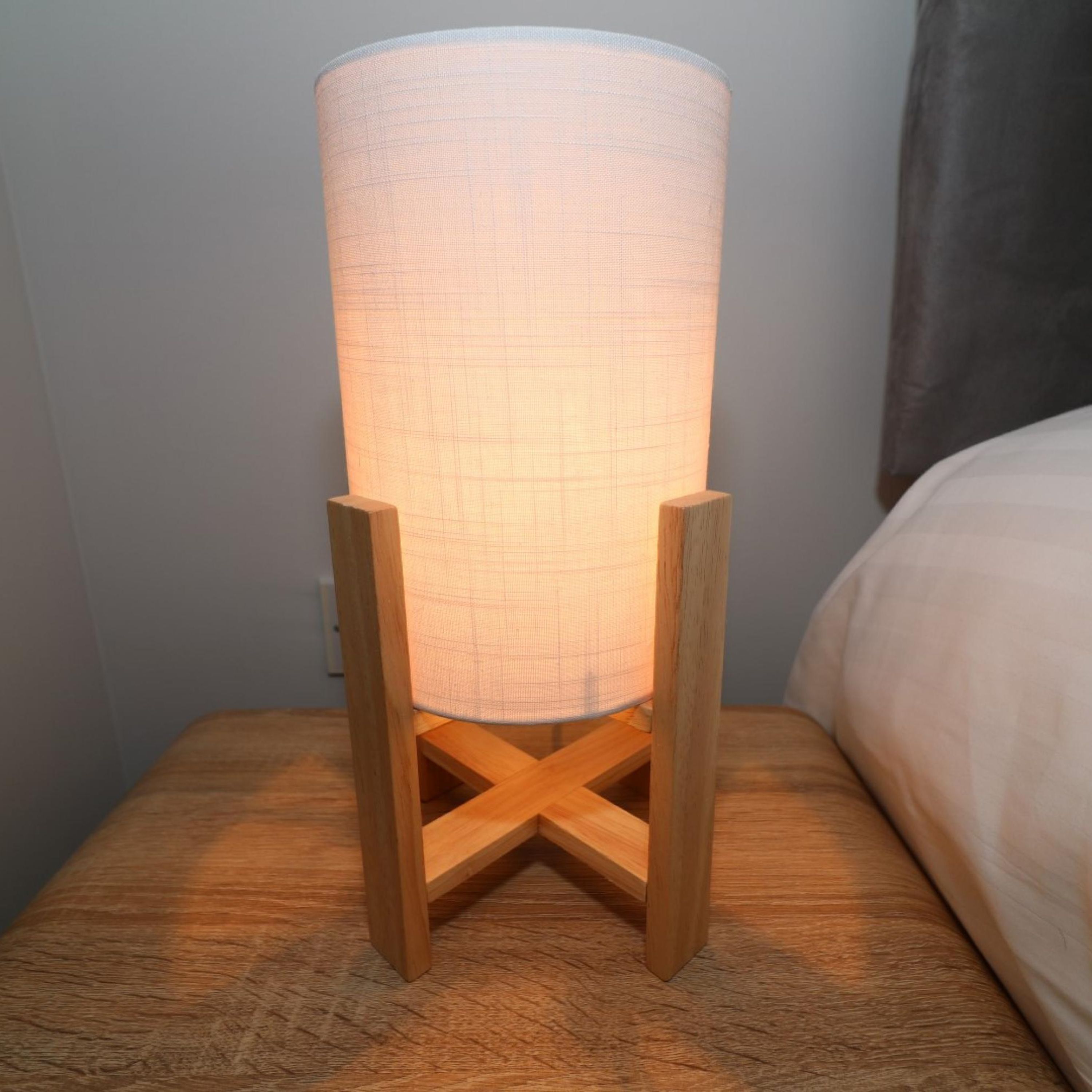 A bedside table with a cylindrical lamp and a wooden base.