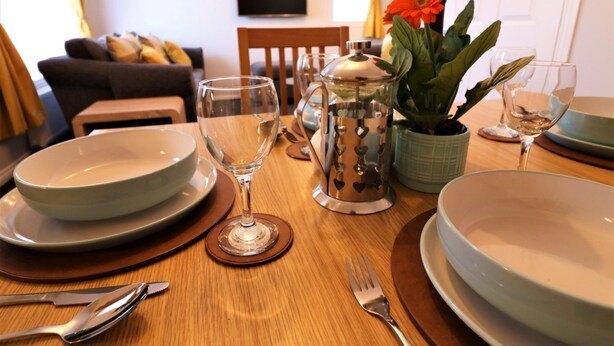 A dining table set with plates, glasses, cutlery, and a decorative pot with flowers. - Connelly House - Motherwell (Motherwell)