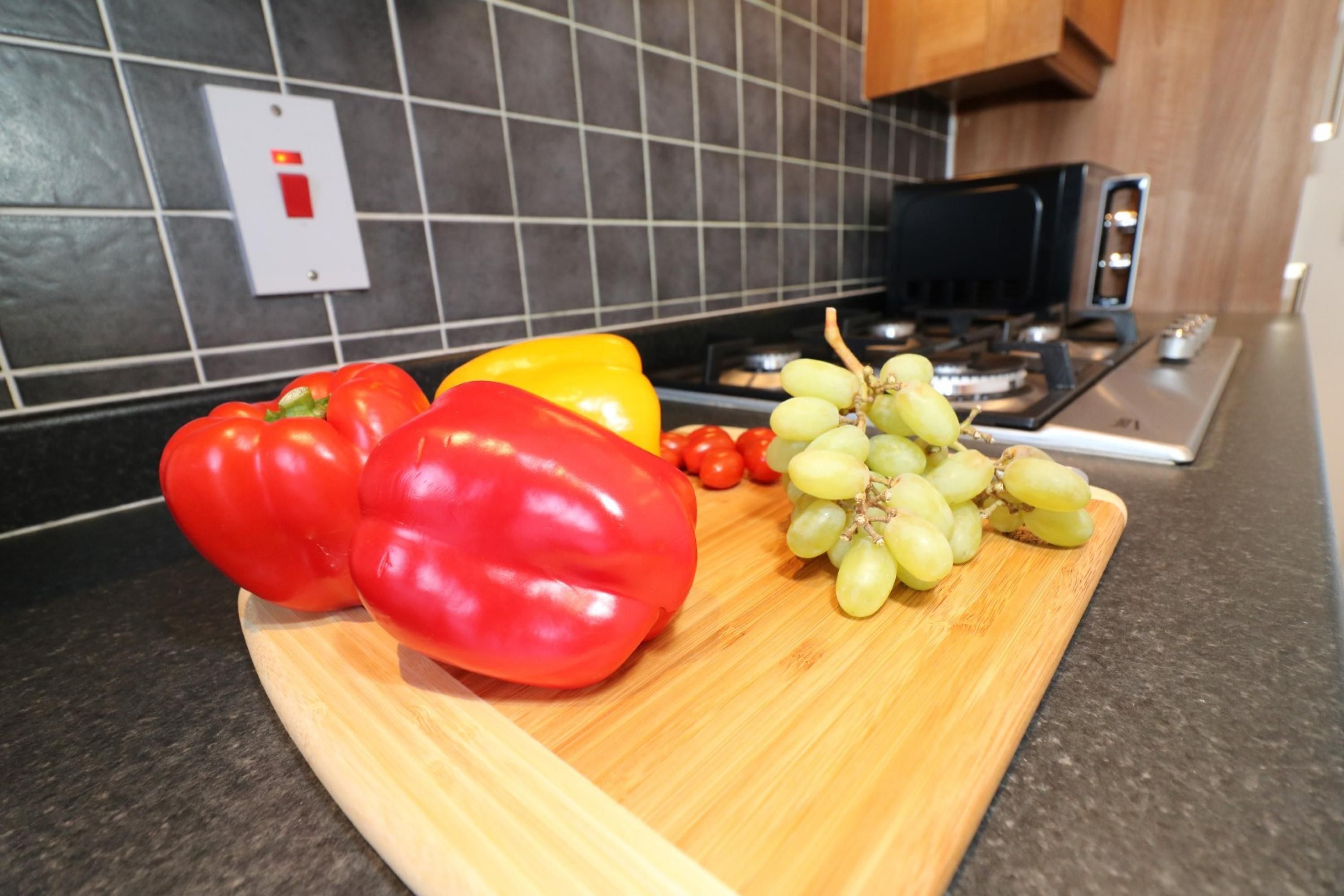 Un plan de travail de cuisine sur lequel se trouve une planche à découper avec des poivrons rouges et jaunes, ainsi qu’une grappe de raisins verts.