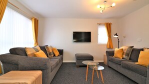 A modern living room with two grey sofas, a wooden coffee table, and a flat-screen TV mounted on the wall. - Connelly House - Motherwell (Motherwell)