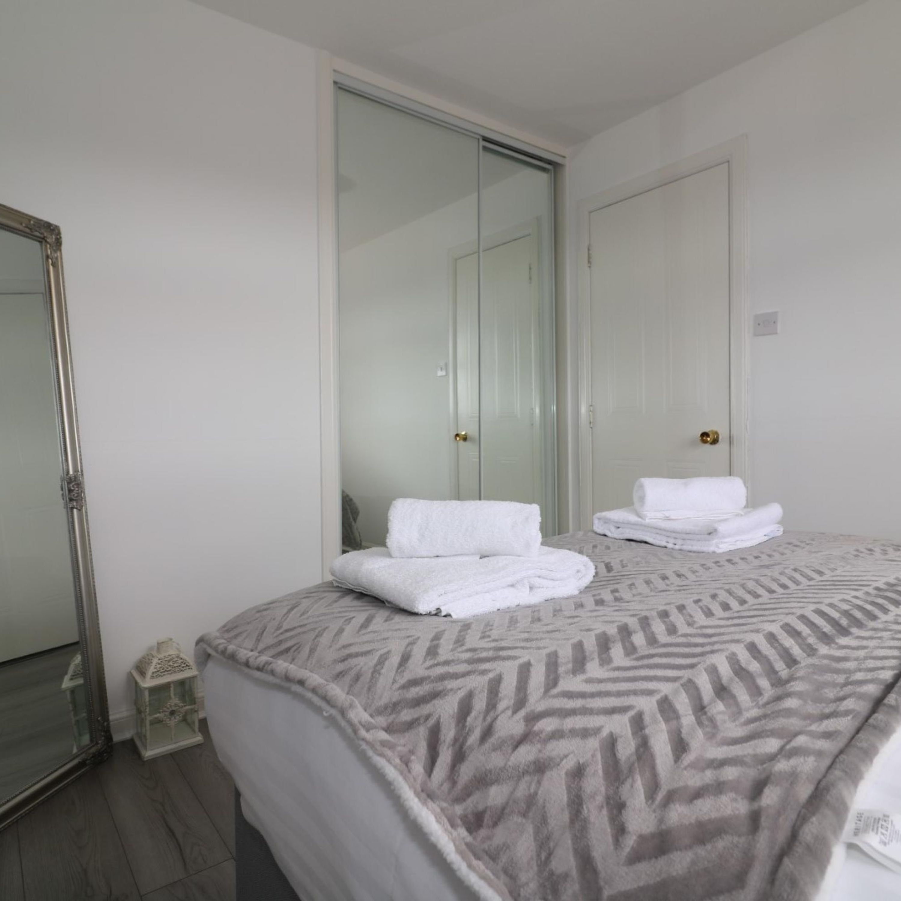 A hotel room with a bed, a large mirror, and a wardrobe.