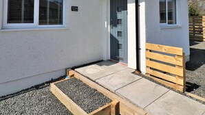 A single-story house with a white exterior, a dark roof, and a small porch with a wooden bench.
