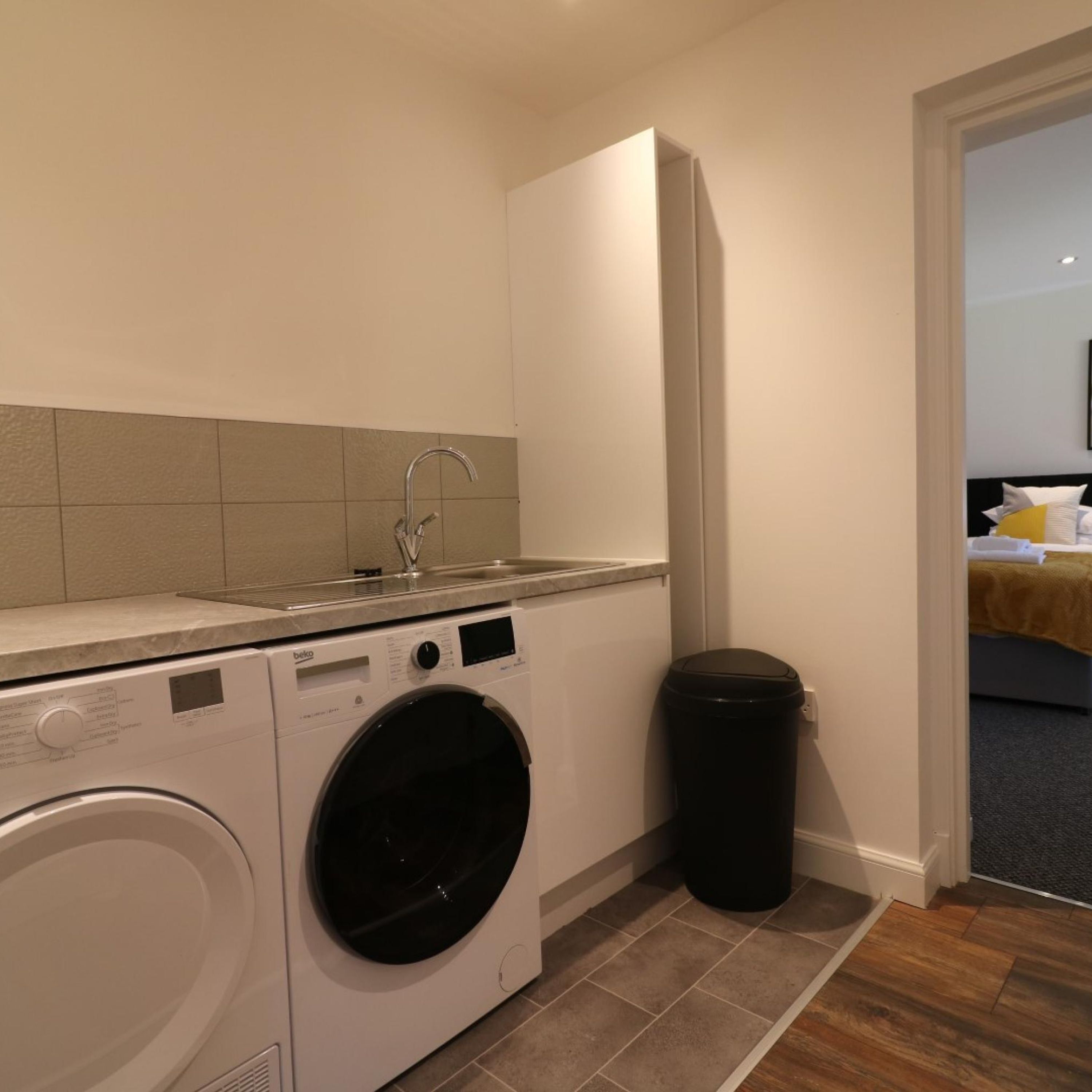 A compact laundry area with a washing machine, a sink, and a trash bin.