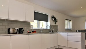 A modern kitchen with white cabinets, a grey backsplash, and a wooden floor.