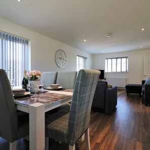 A modern dining area with a table set for two, a sofa, and a TV in the background.