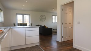 A modern kitchen with white cabinetry, a dining area with a dark sofa, and a large wall clock.