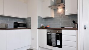 Una cocina moderna con armarios blancos, horno empotrado, microondas y campana extractora de acero inoxidable.