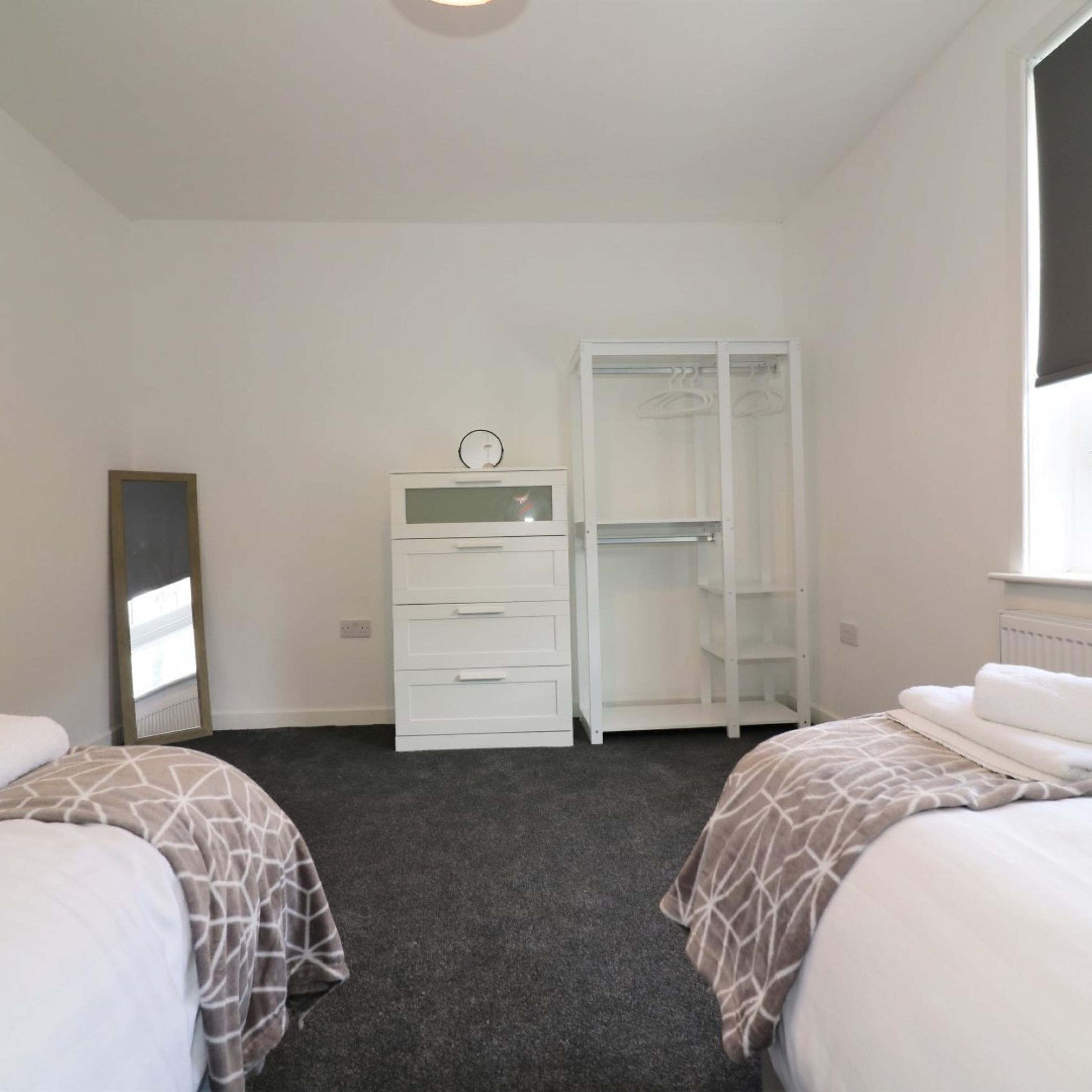 A hotel room with two beds, a white wardrobe, a mirror, and a window.