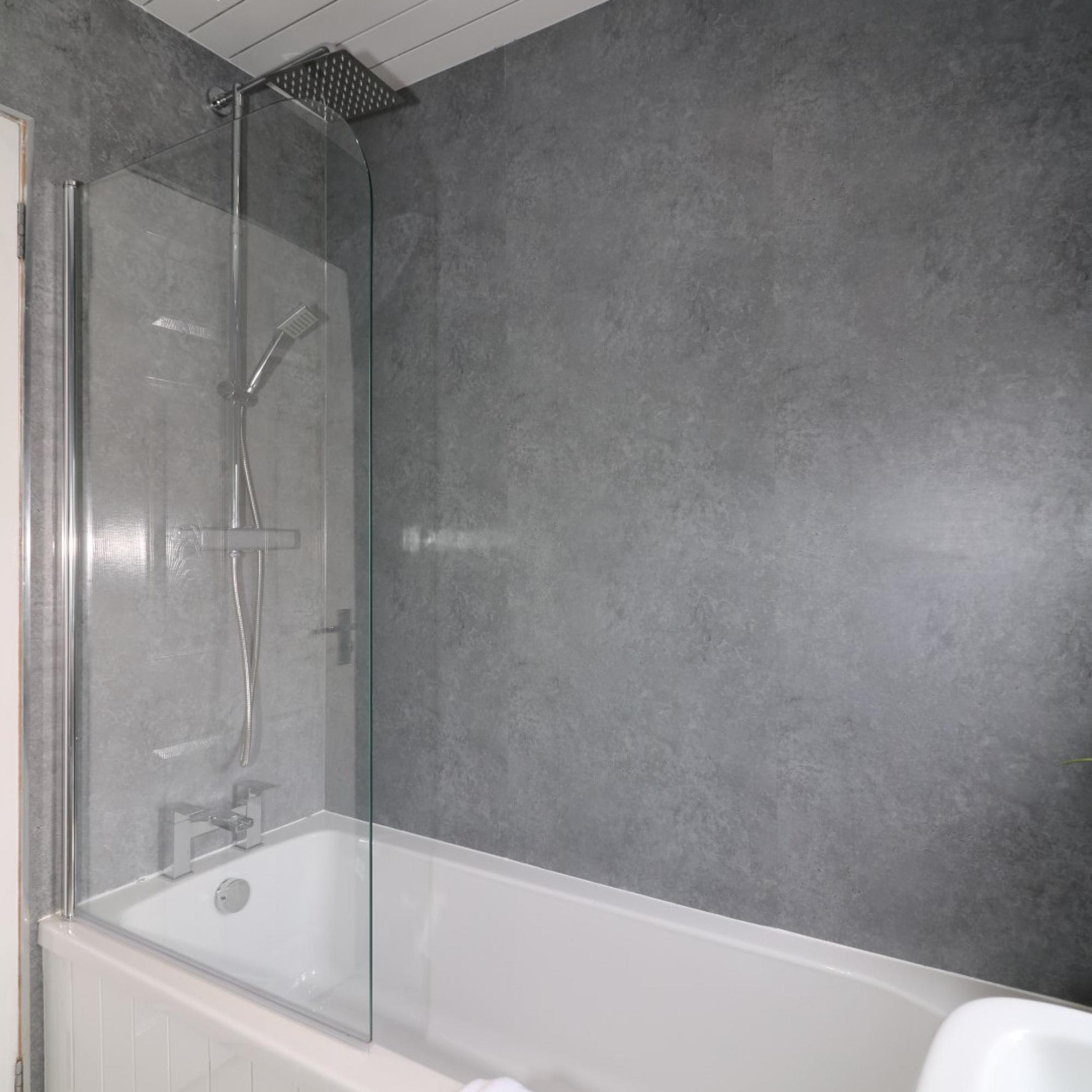 Une salle de bain moderne avec une douche à parois de verre, une baignoire blanche et un mur gris à texture.