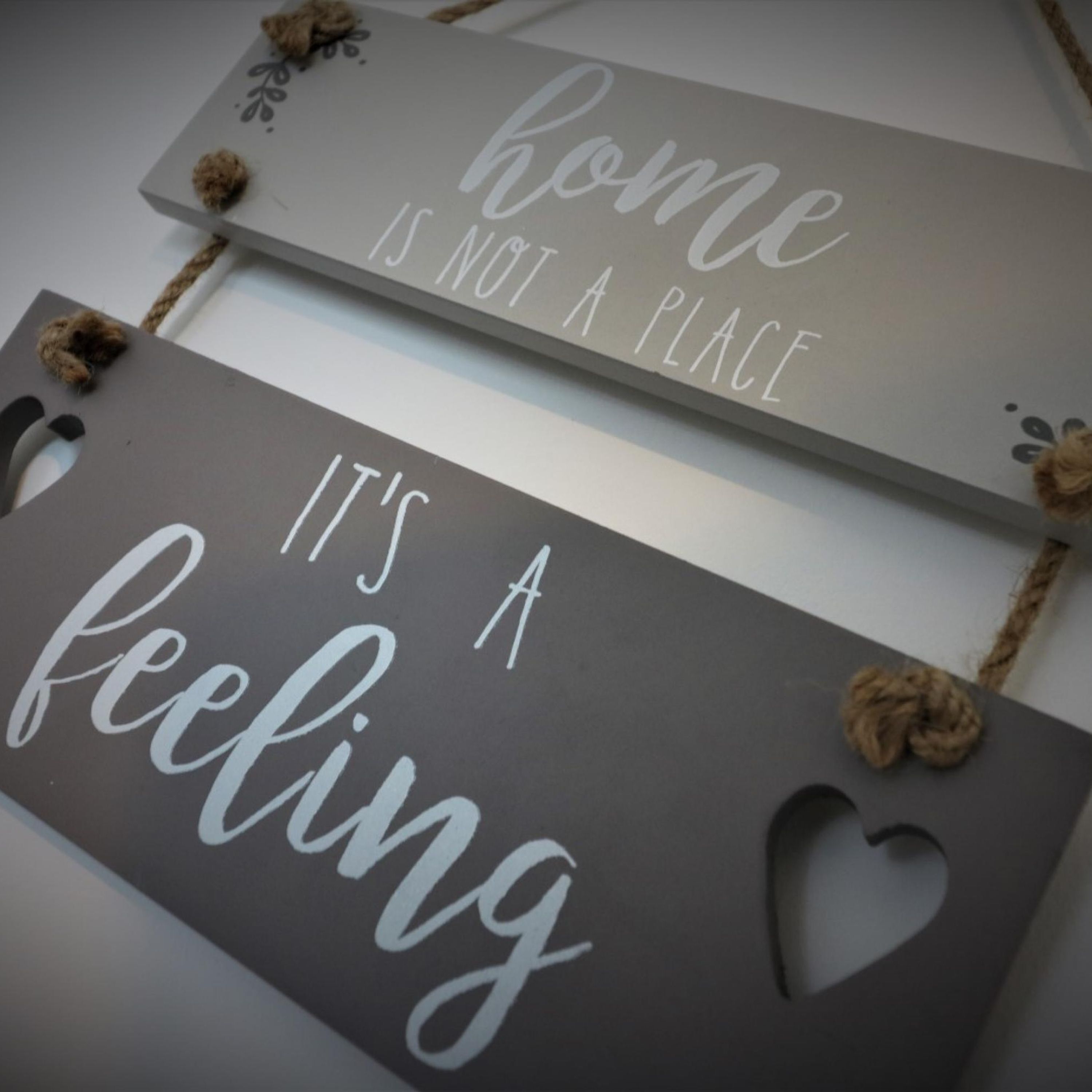 Two signs with the text "home is not a place" and "it's a feeling" hanging on a wall.