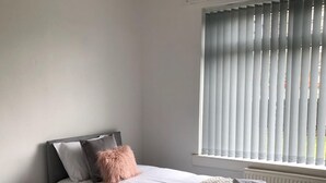 Un dormitorio con cama, mesita de noche y ventana con persianas.