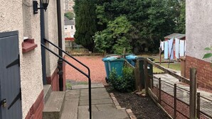 Un sendero estrecho que conduce a un edificio con barandilla metálica y una puerta.