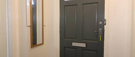 A dark grey door with a small window and a nameplate, white walls, and a mirror on the adjacent wall.