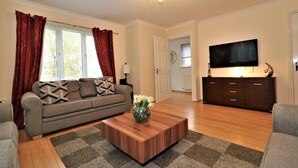 Un salon comprenant un canapé, une table basse avec un vase, un téléviseur à écran plat et un meuble en bois.
