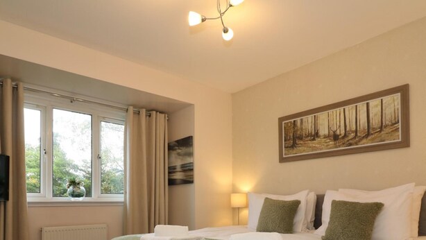 Une chambre d’hôtel avec un grand lit, un tableau au mur, une fenêtre avec des rideaux et un radiateur.