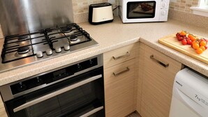 Cocina compacta con estufa a gas, horno, microondas, tostadora y tabla de madera con tomates.