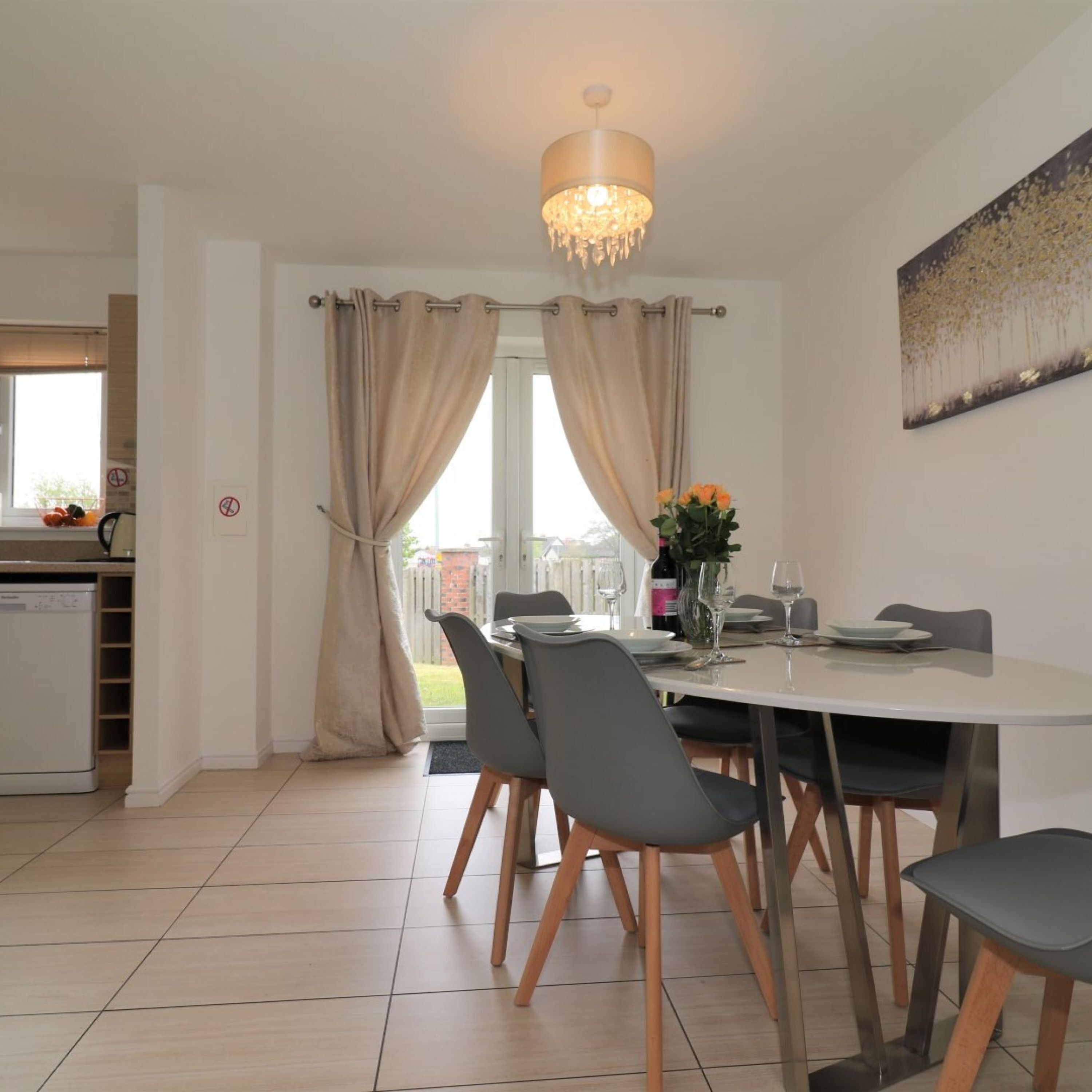 A modern dining area with a round table, grey chairs, and a chandelier.