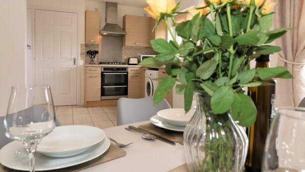 Una mesa de comedor lista con platos, cubiertos y un florero.