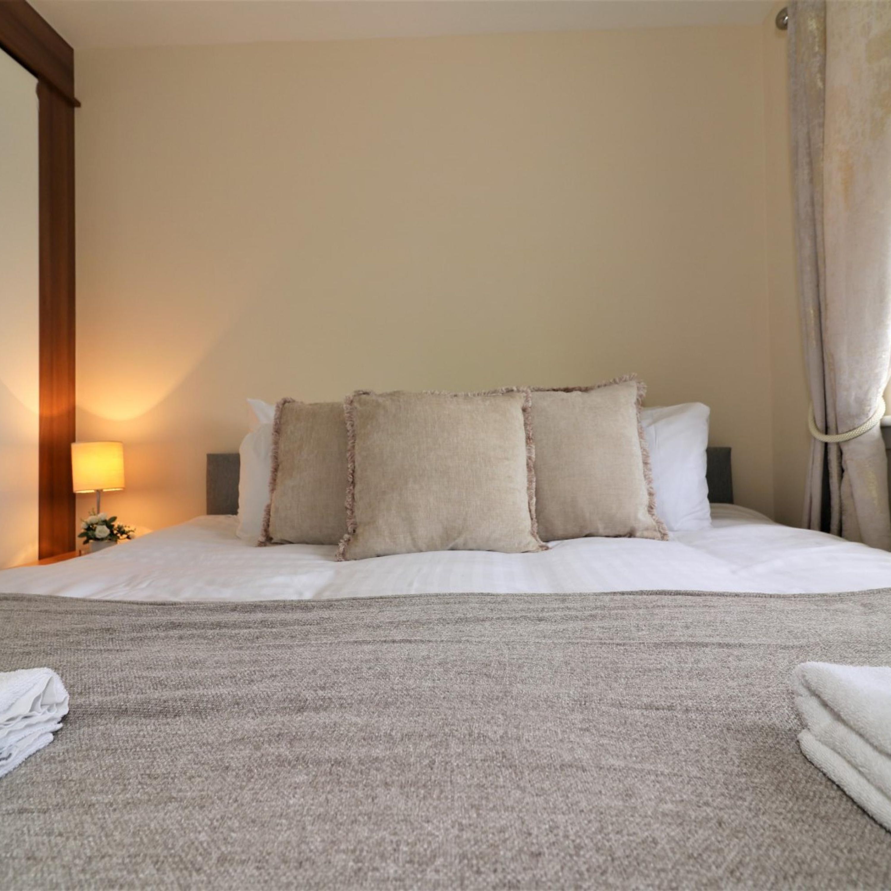 A neatly made bed with a grey blanket, two beige pillows, and a white pillow.