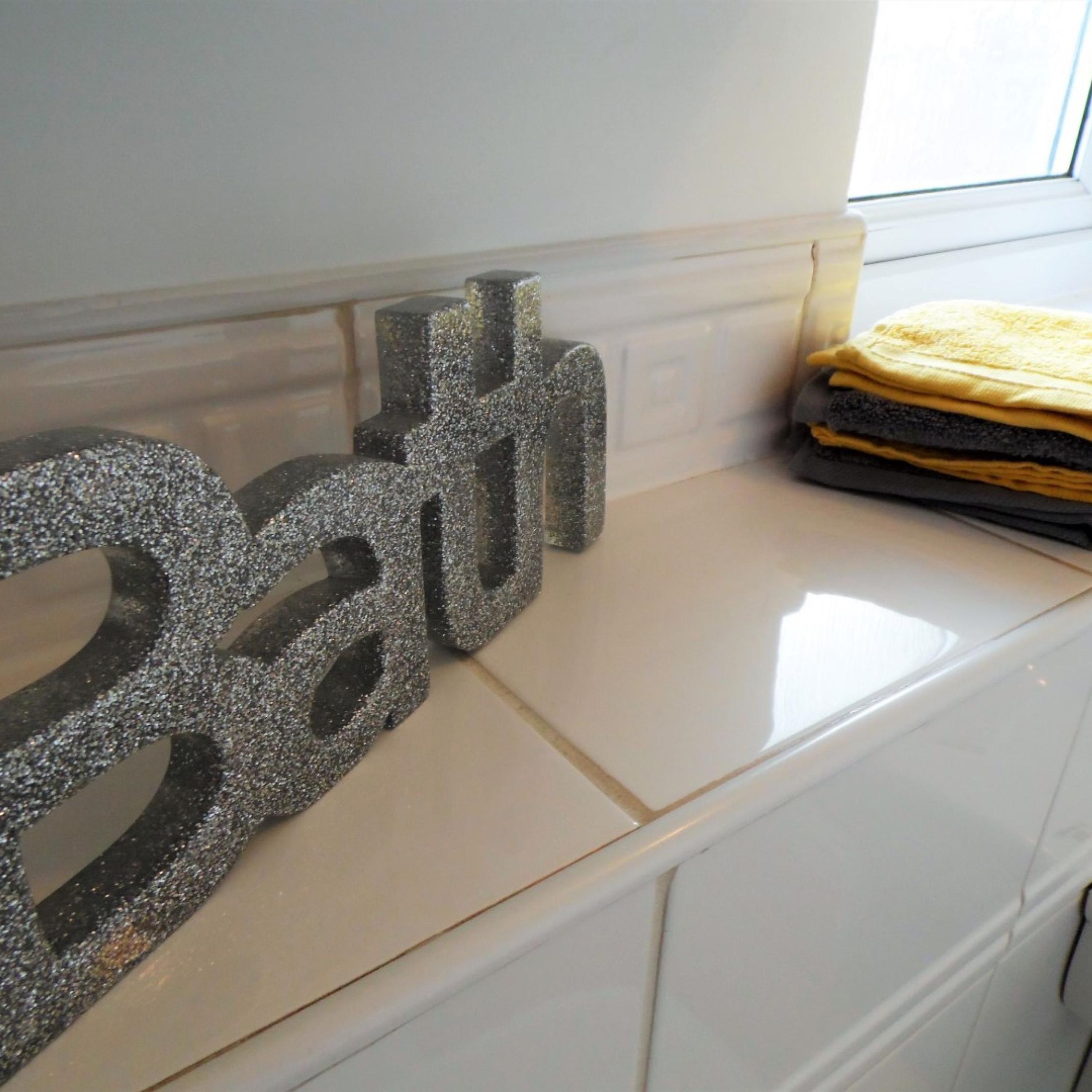 Una encimera de cocina con una letra 'H' plateada decorativa y una pila de toallas amarillas dobladas.