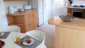 Une cuisine avec des meubles en bois, un réfrigérateur blanc, une cuisinière et une table à manger avec des sets de table et un muffin.