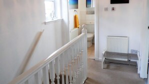 Un couloir avec un escalier blanc, un radiateur et une grille de radiateur.