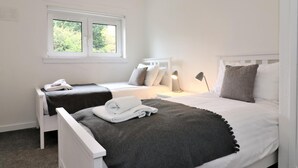 A bedroom with a bed, two bedside tables, a window, and a wall-mounted light fixture. - Belhaven House - Hamilton (Hamilton)