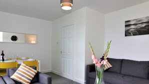 A modern living room with a grey sofa, a glass coffee table, and a decorative vase with flowers. - Belhaven House - Hamilton (Hamilton)