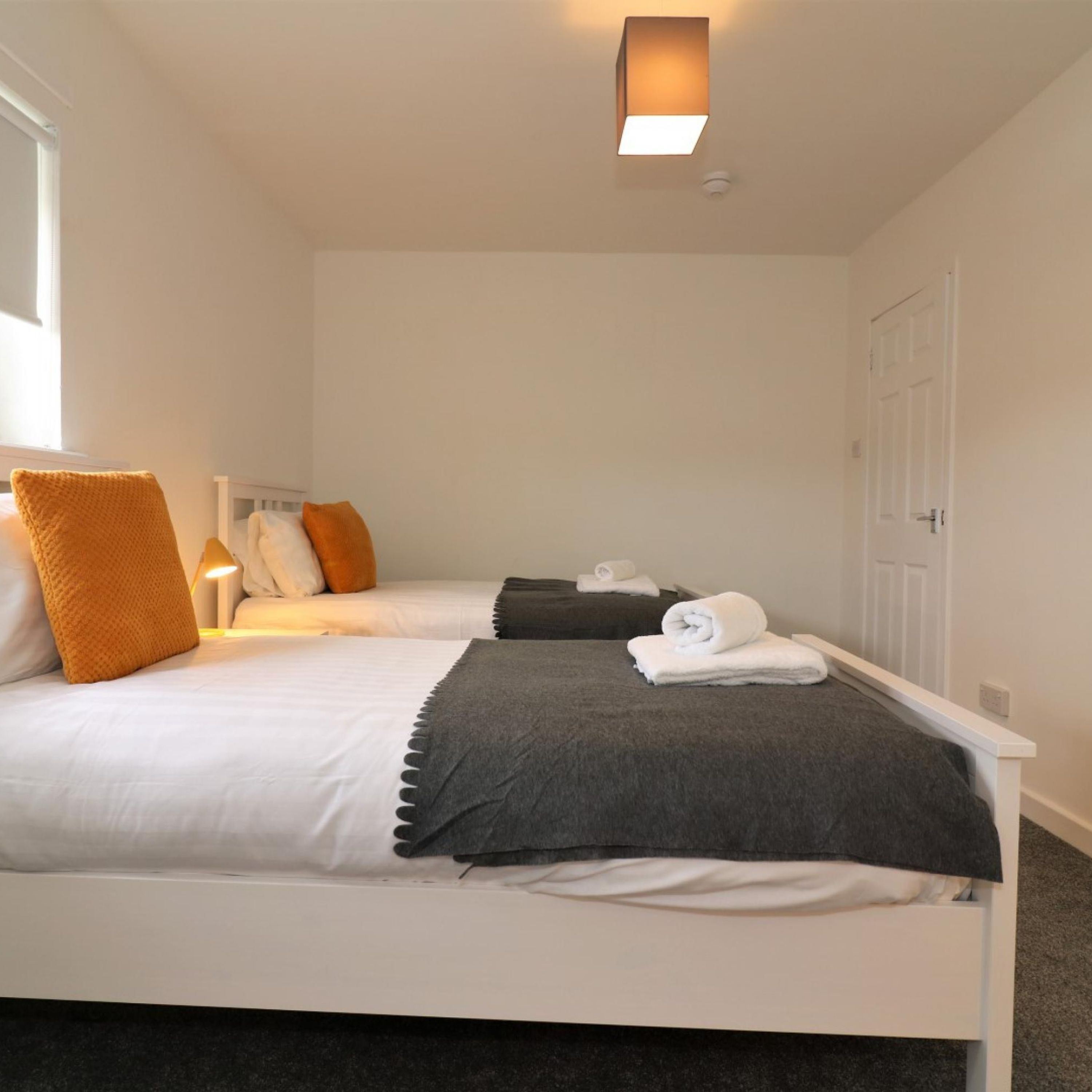 A hotel room with two beds, white bedding, a grey throw, and a bedside lamp.