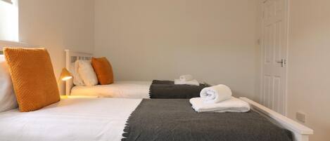A hotel room with two beds, white bedding, a grey throw, and a bedside lamp.