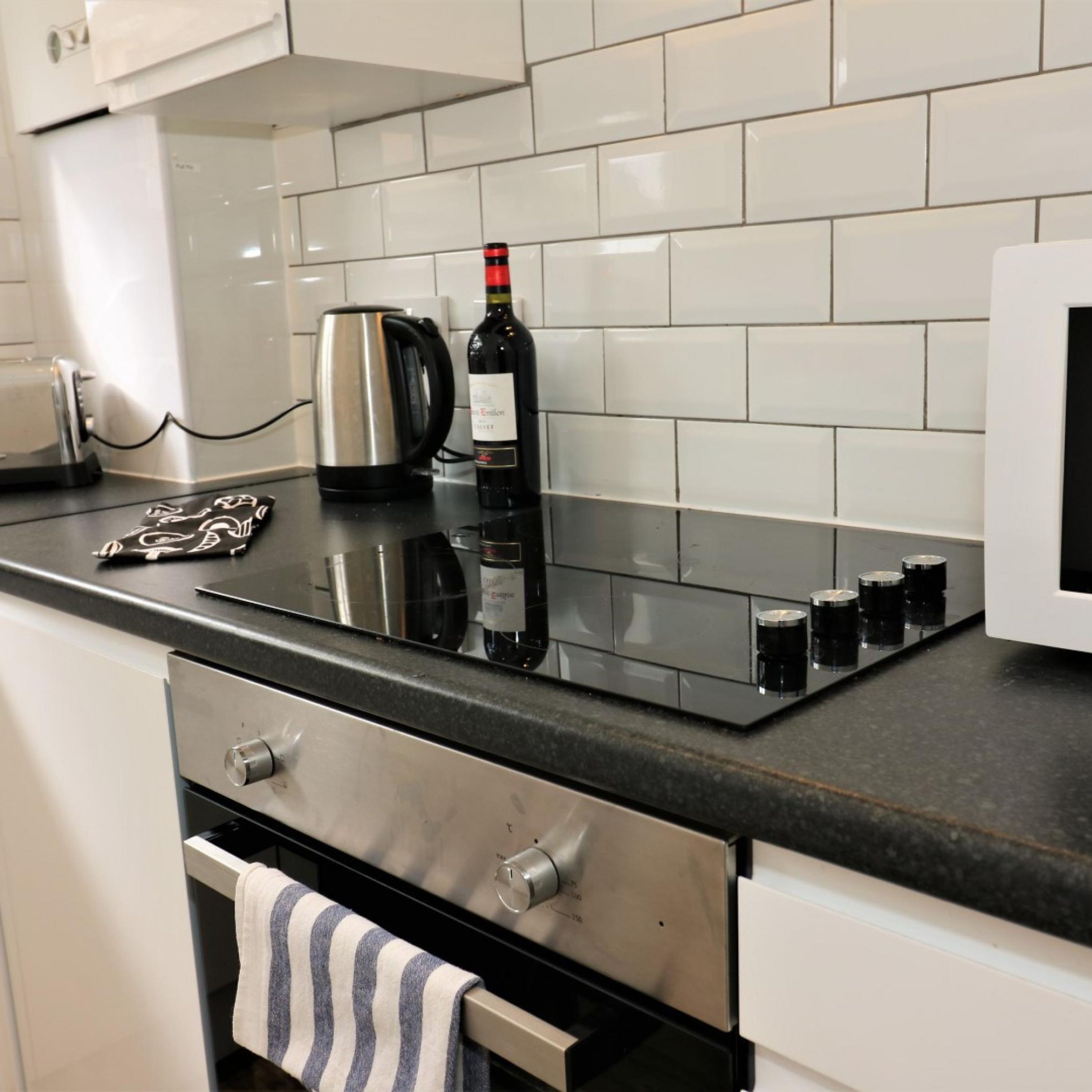 A modern kitchen with a black countertop, stainless steel appliances, and a wine bottle.