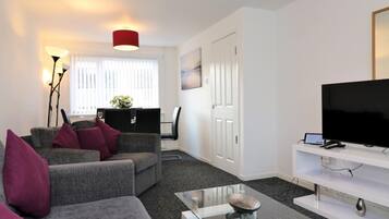 A modern living room with a grey sofa, a glass coffee table, a flat-screen TV, and a red pendant light.