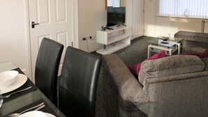 A modern living room with a flat-screen TV, a glass coffee table, and a grey sofa. - Atholl House - Linwood (Paisley)