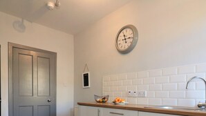 Een moderne keuken met witte kastjes, een houten aanrecht, een klok en een betegelde achterwand.