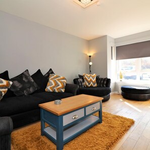 A living room with a black sofa set, a wooden coffee table, and a patterned rug. - Whistleberry House - Hamilton (Hamilton)