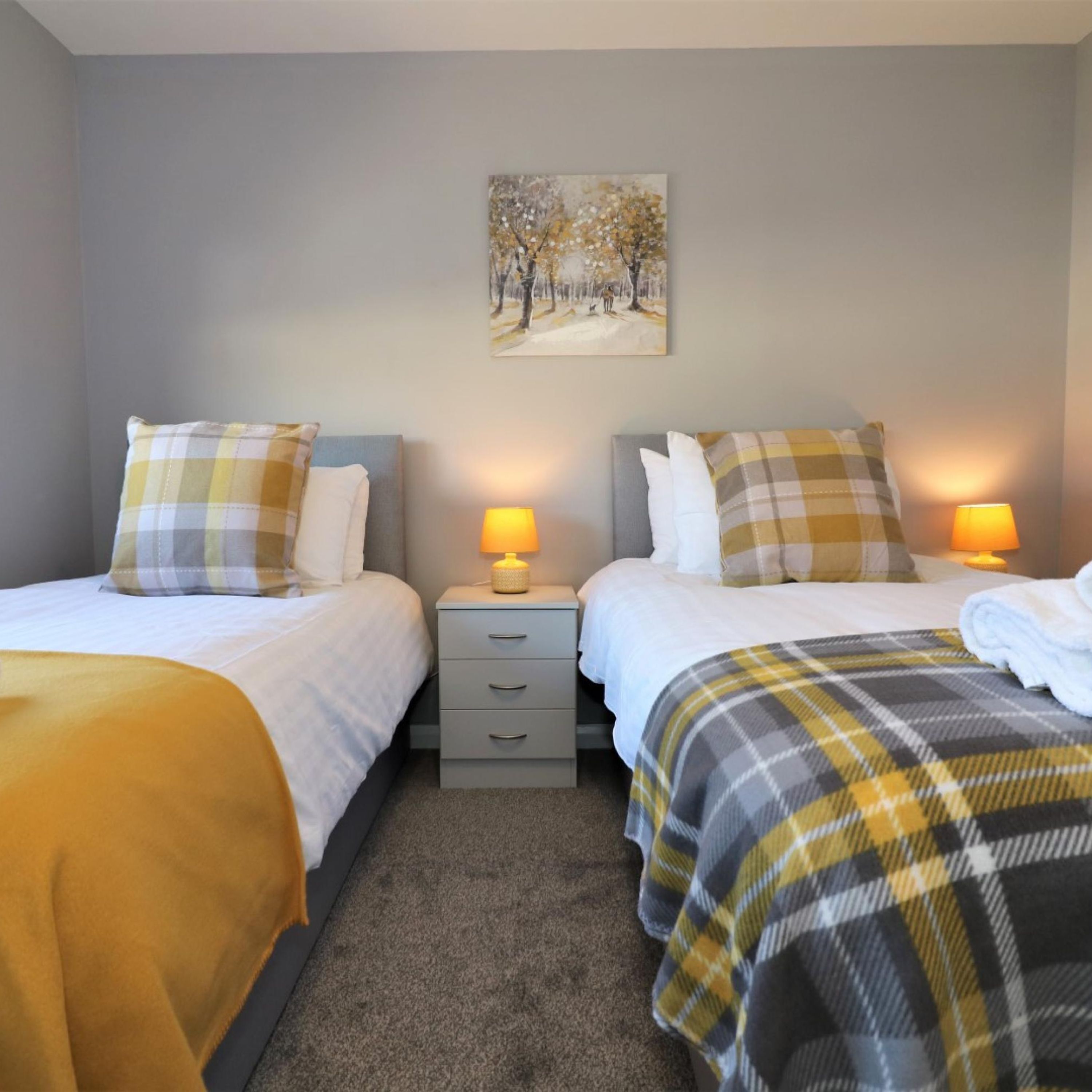 Ein Hotelzimmer mit zwei Betten, einem Nachttisch, einer Lampe und einem Gemälde an der Wand.