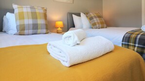 Ein Hotelzimmer mit zwei Betten, jedes mit einer gelb-weißen Karodecke, weißen Kissen und einem Baumgemälde an der Wand.