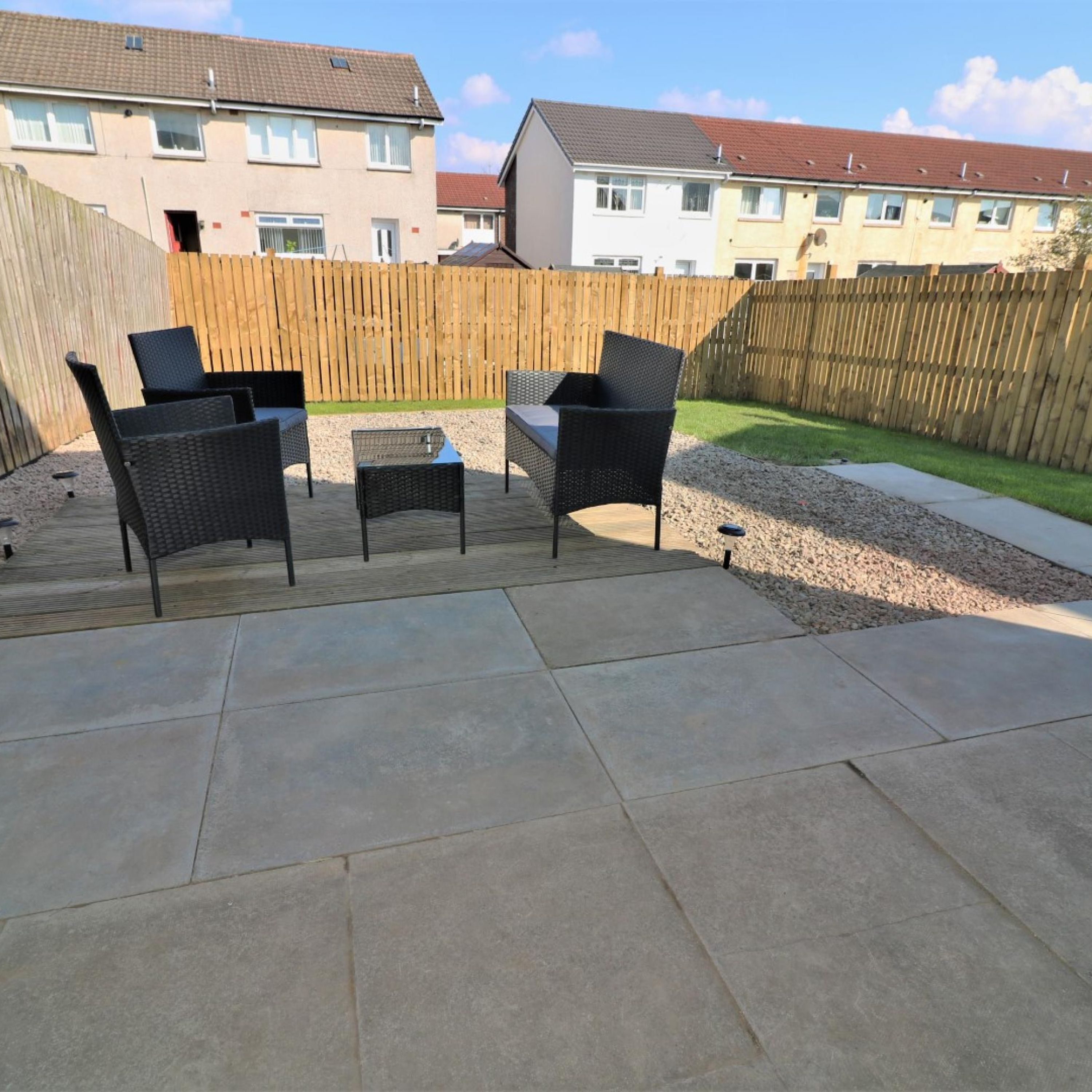 Eine Terrasse mit Gartenmöbeln, einem Holzzaun und einem Kiesweg.
