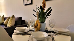 Un comedor con una mesa dispuesta para dos personas, con platos blancos, cubiertos y una botella de champán.