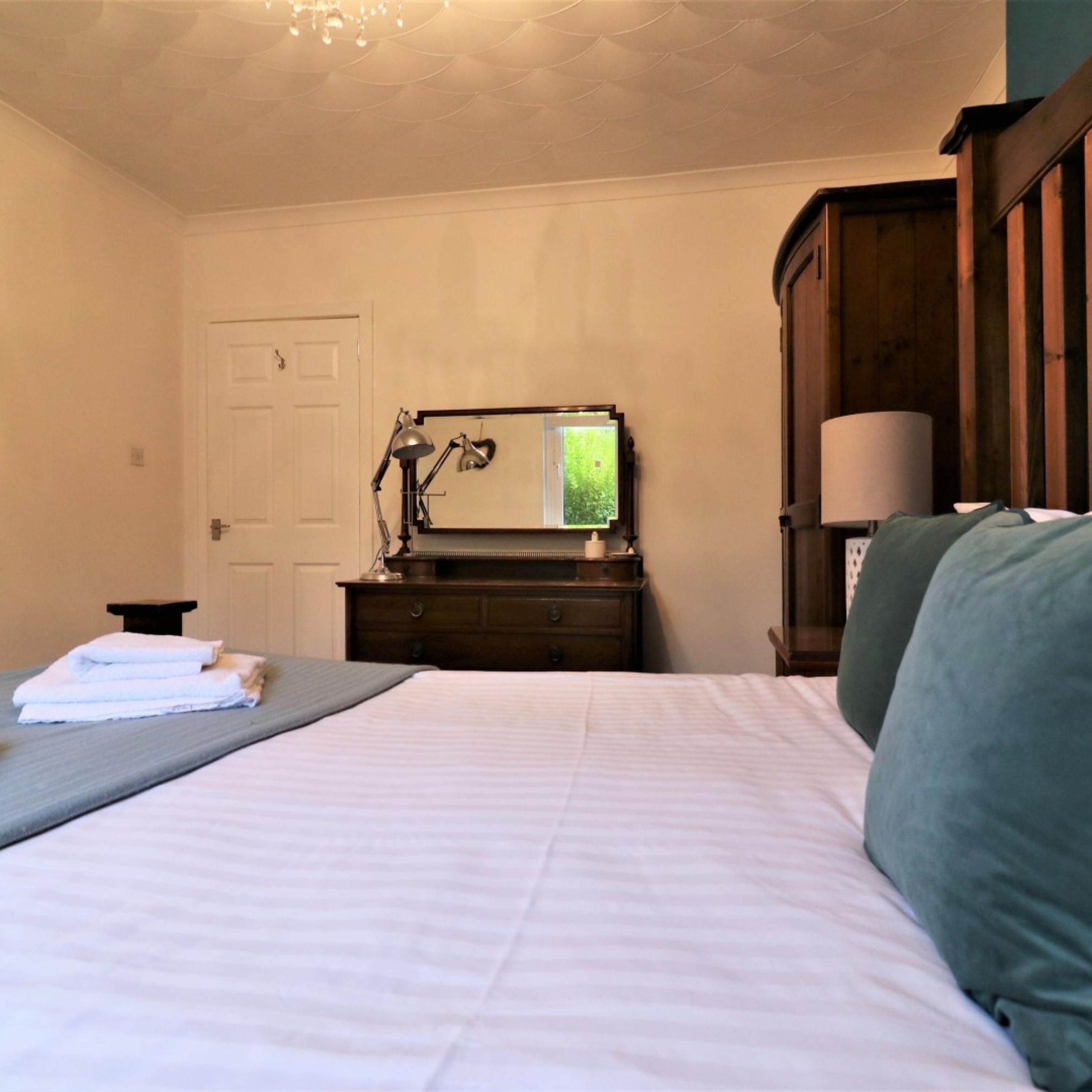 A bedroom with a bed, a dresser, a mirror, and a lamp.
